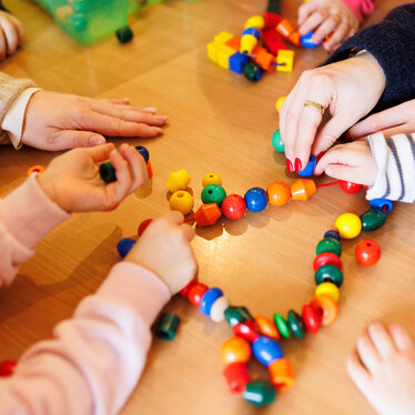 Kinderhände zusammen in einer Kita Kinderhände in einer Kita legen gemeinsam eine Reihe aus Kugeln. Ein gutes Beispiel für Bildungsangebote für Kinder in Kita und Gemeinde.